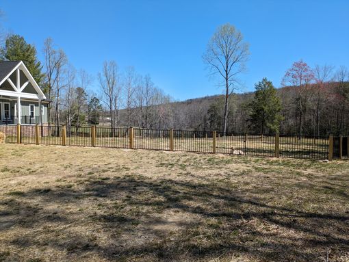 A wooden fence surrounds a grassy field in front of a house.