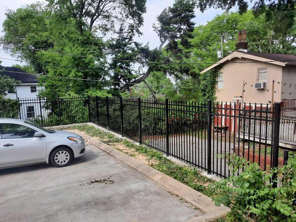 A white car is parked in a parking lot next to a fence.
