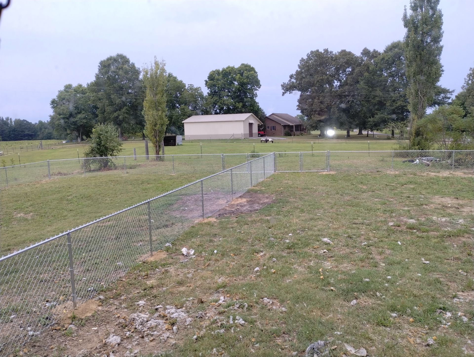 A fence surrounds a grassy field with a barn in the background