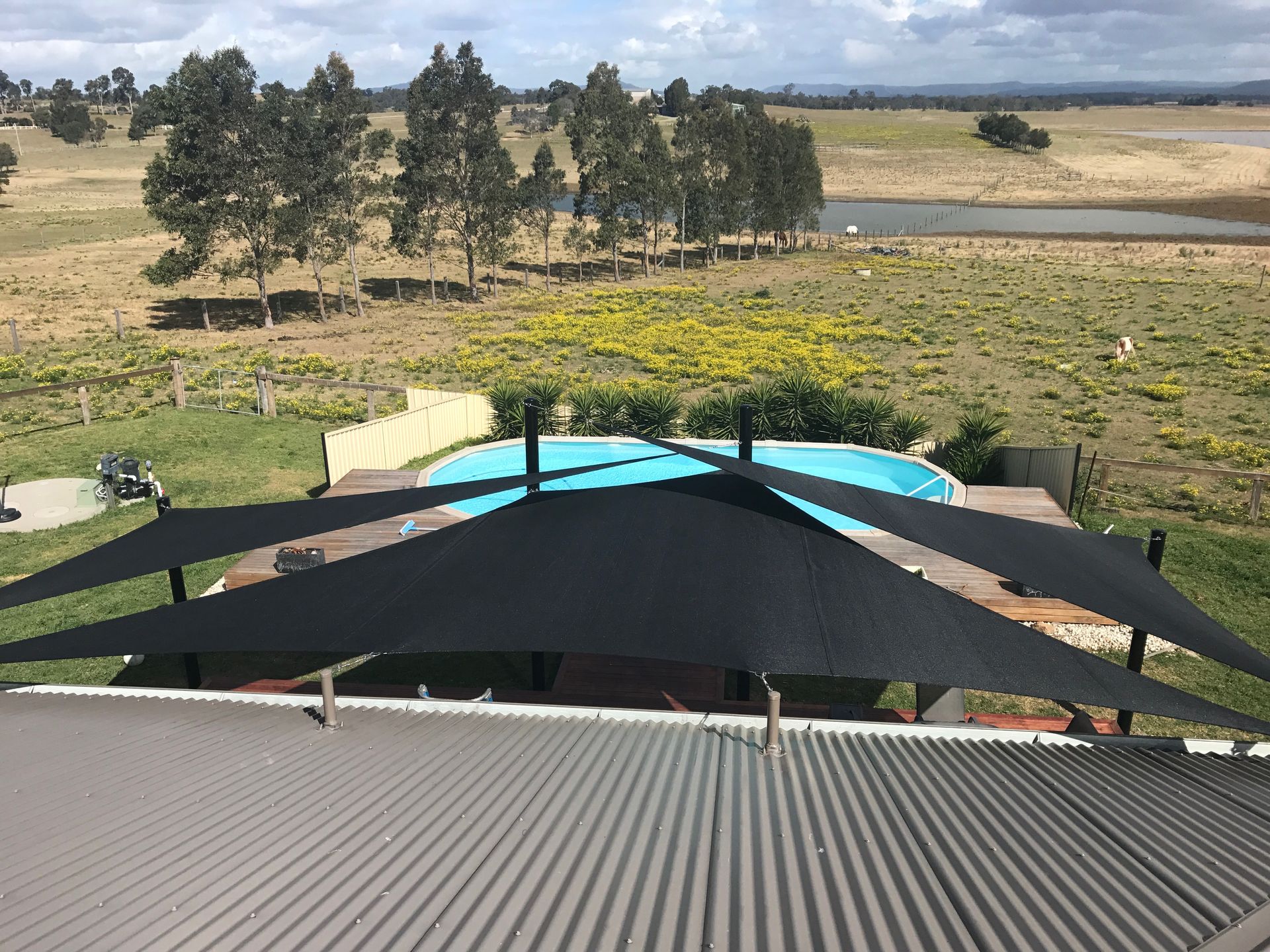 Black shade sails over a backyard pool, viewed from a corrugated metal roof overlooking a rural landscape — Shades of Blue In North Wyong, NSW