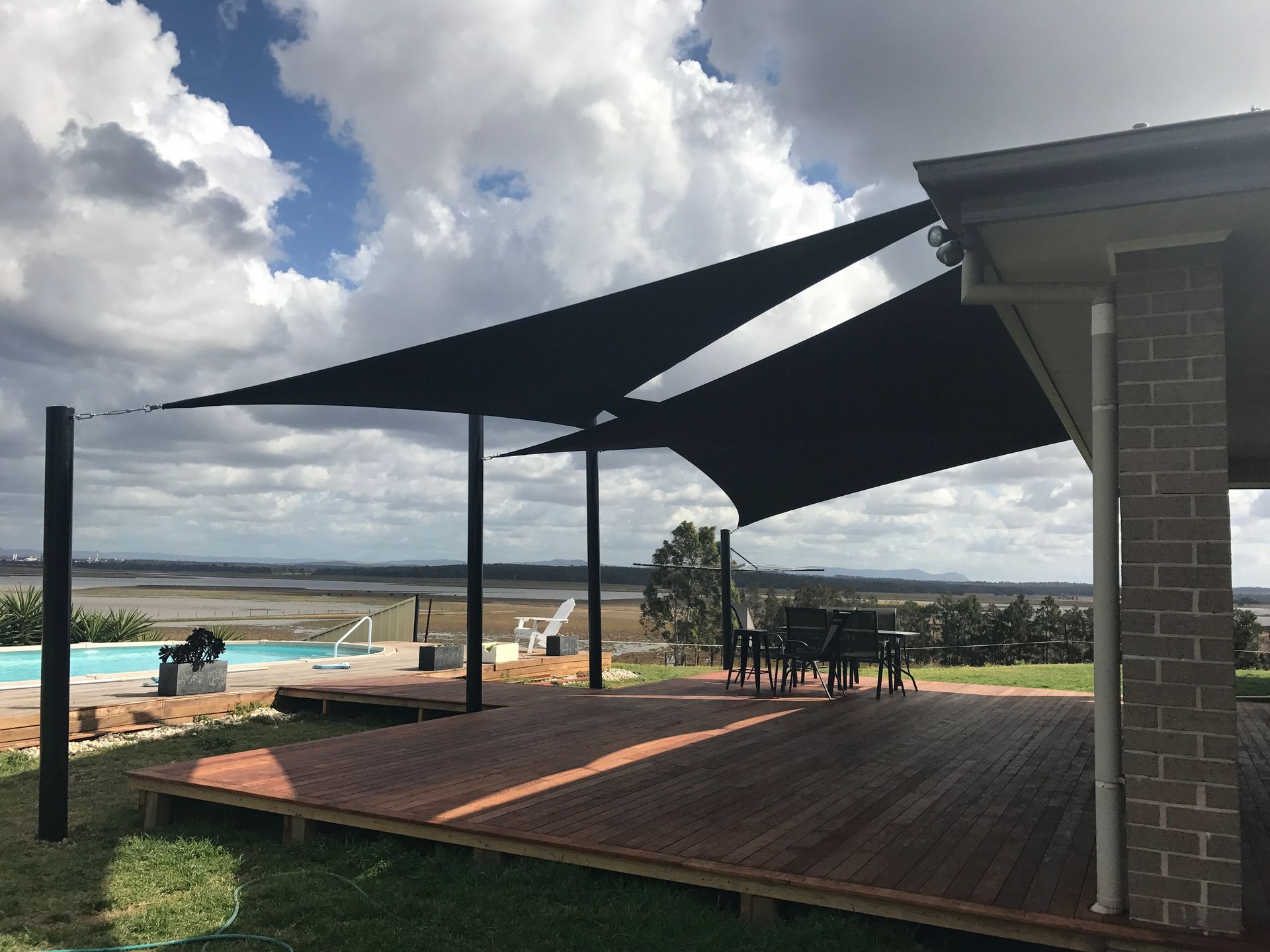 Two large black shade sails installed over a wooden deck beside a swimming pool, overlooking a distant landscape — Shades of Blue In North Wyong, NSW