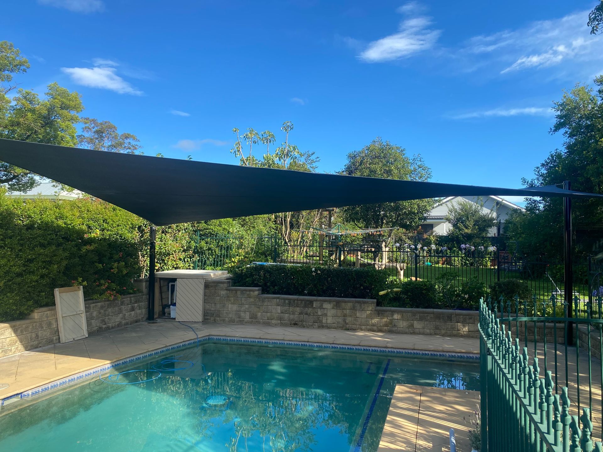 A rectangular black shade sail installed over a backyard swimming pool under a bright blue sky — Shades of Blue In North Wyong, NSW