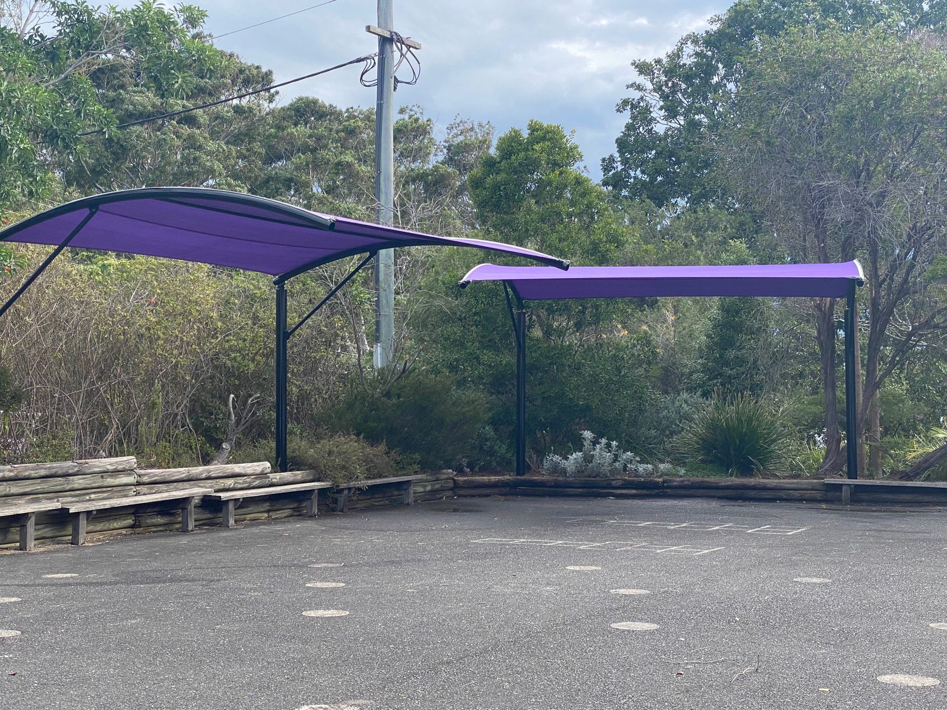 Two purple shade sails covering a bench area in a park with trees and a gravel ground — Shades of Blue In North Wyong, NSW
