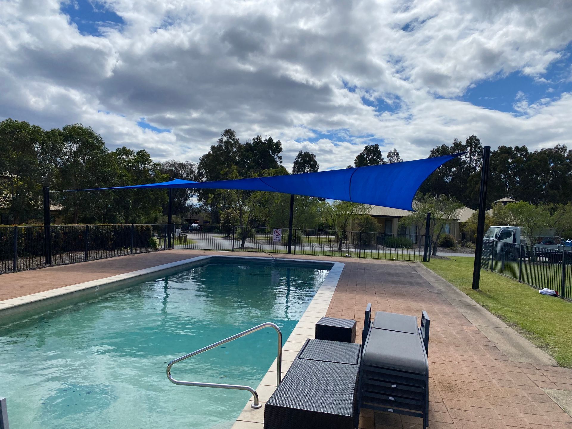 A blue shade sail covers a backyard swimming pool with lounge chairs on the patio under a cloudy sky — Shades of Blue In North Wyong, NSW