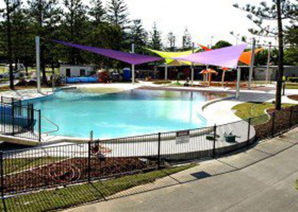 A blue swimming pool in a park, surrounded by a metal fence and shaded by colorful, triangular fabric sails — Shades of Blue In North Wyong, NSW