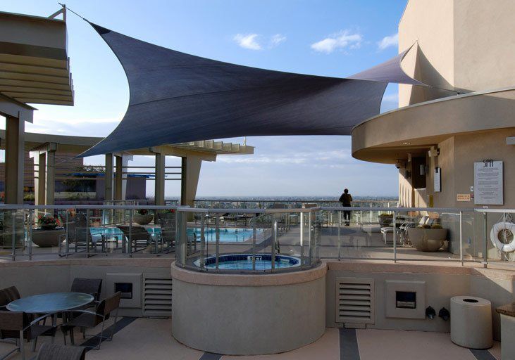 A rooftop patio with a lounge pool, a hot tub, seating areas, and a large triangular shade sail against a cityscape. — Shades of Blue In North Wyong, NSW