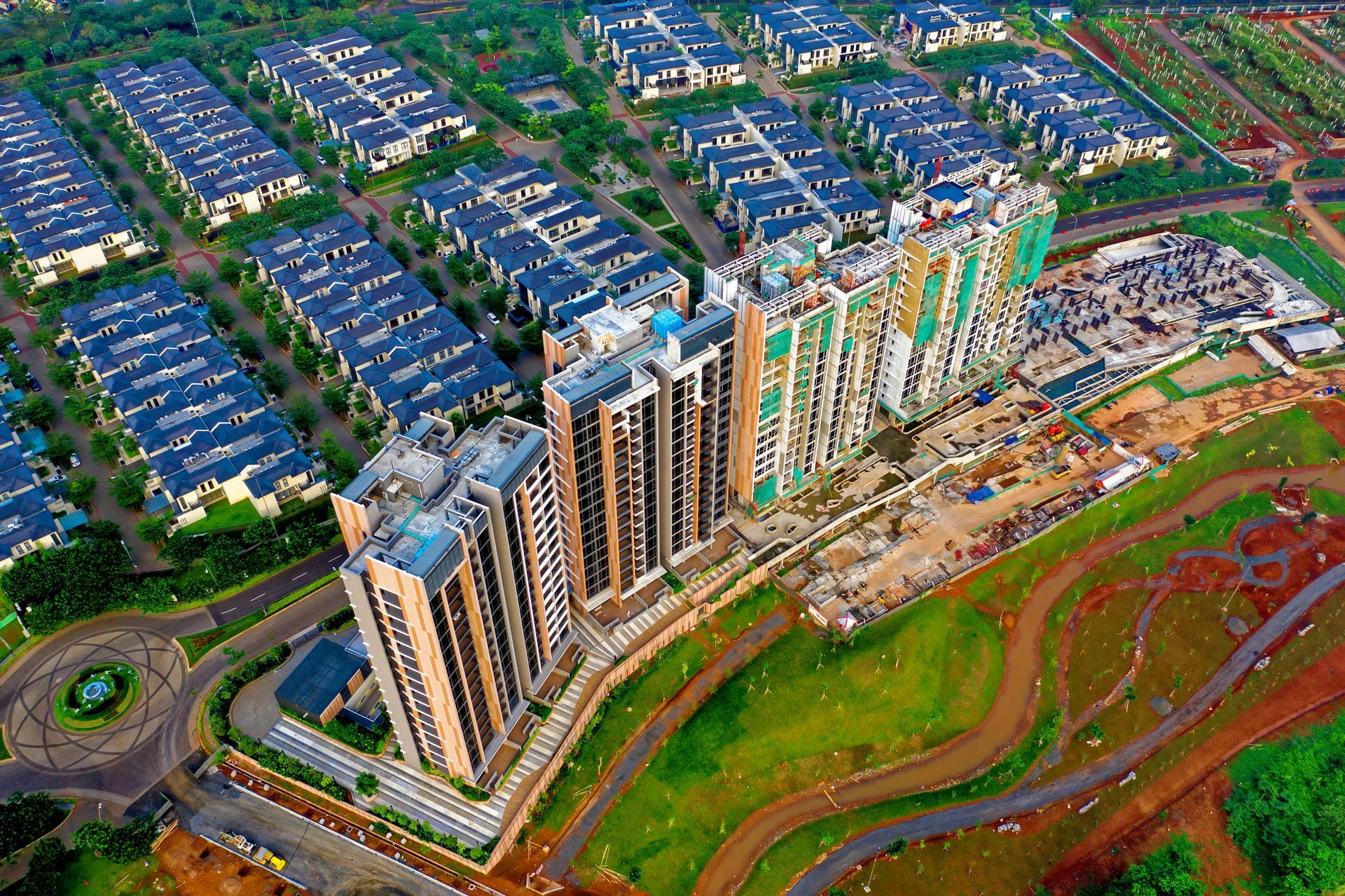 Aerial view of a modern city with tall residential towers and rows of houses, surrounded by green spaces.