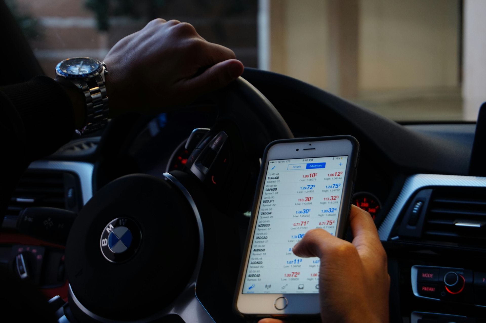 Person using a phone displaying a trading app while driving a BMW.
