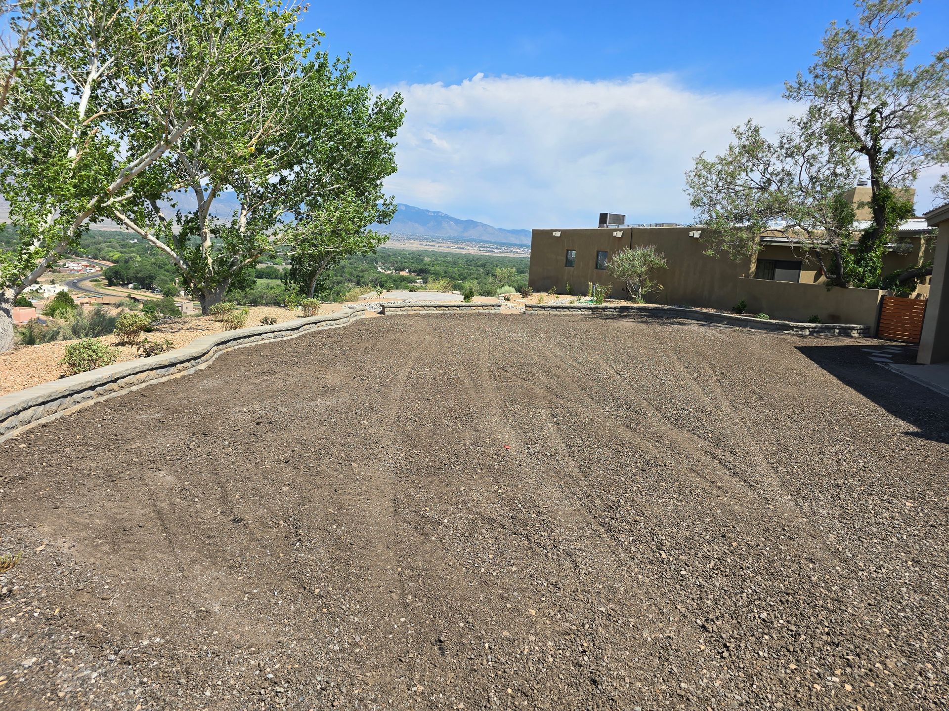 A gravel driveway with trees and mountains in the background