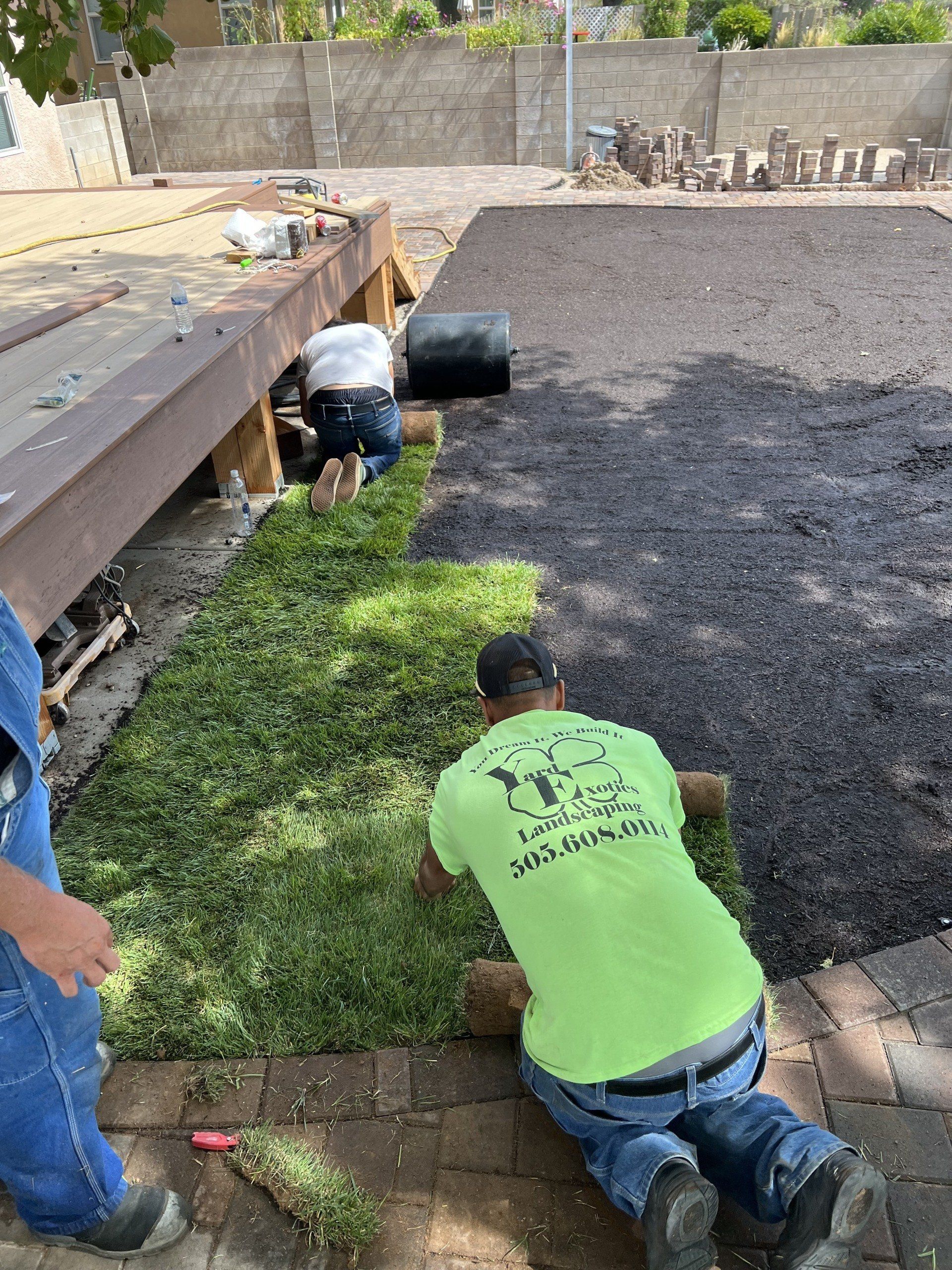 A man in a neon green shirt is kneeling down in front of a pile of grass.
