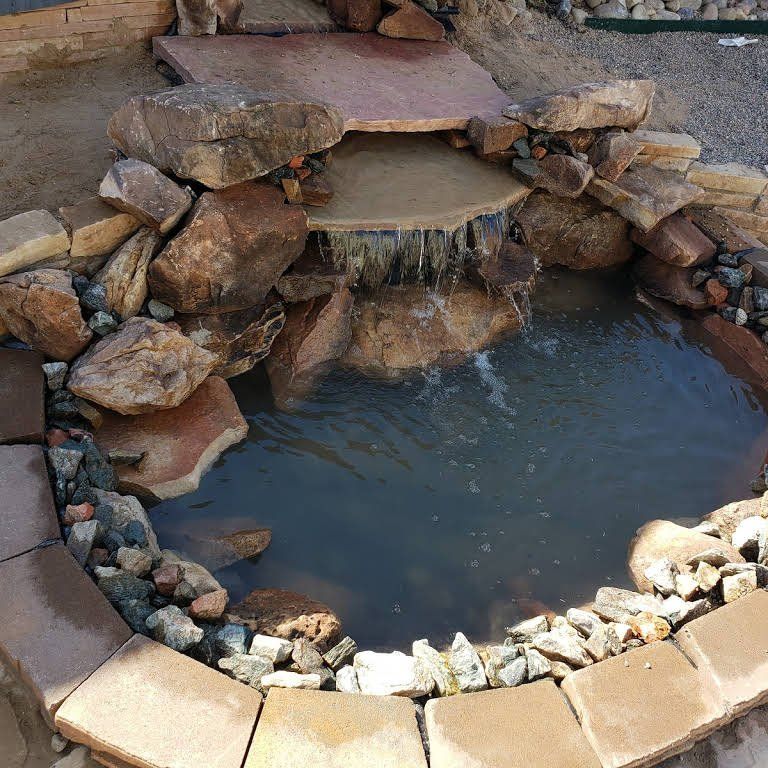 A small waterfall is surrounded by rocks and bricks