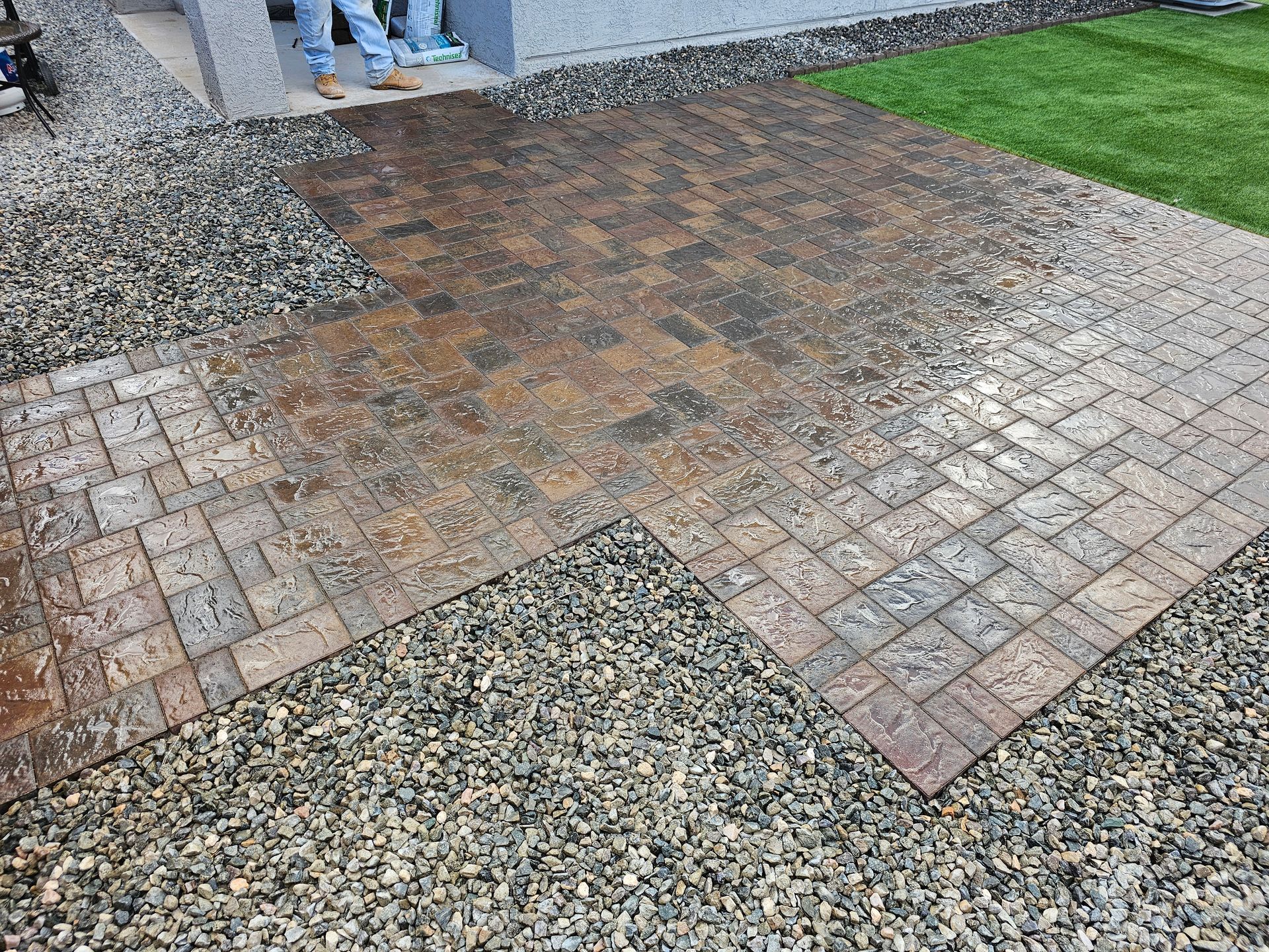 A man is standing on a brick walkway next to a gravel driveway.