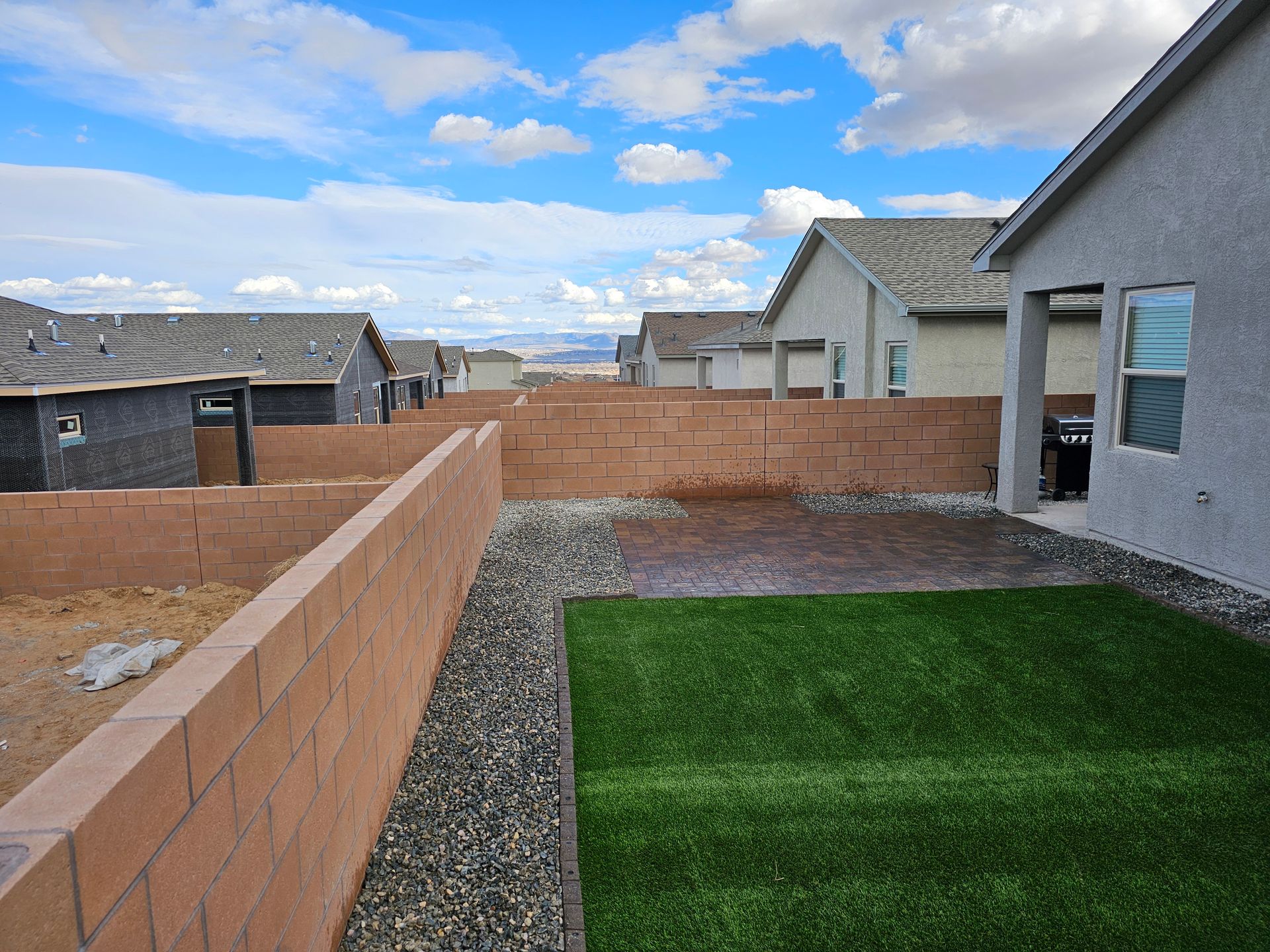 A backyard with a brick wall and a lawn in front of a house.