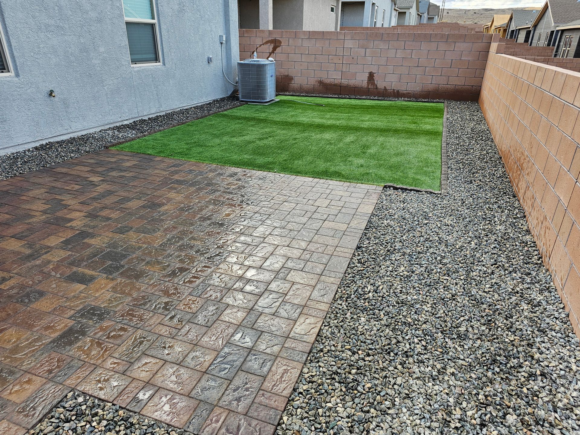 A backyard with a brick walkway and a grassy area.