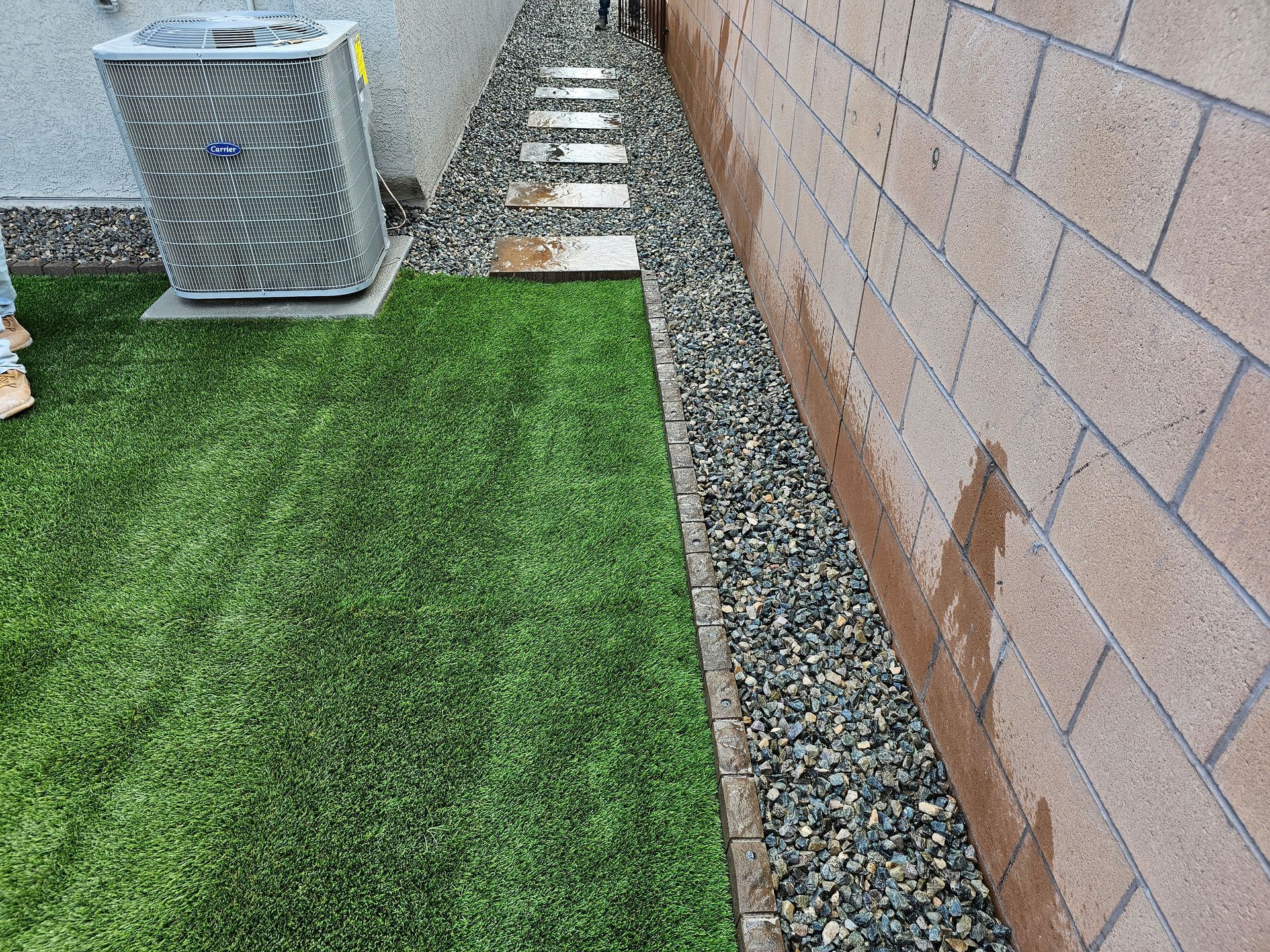 A person is standing in the grass next to a brick wall.