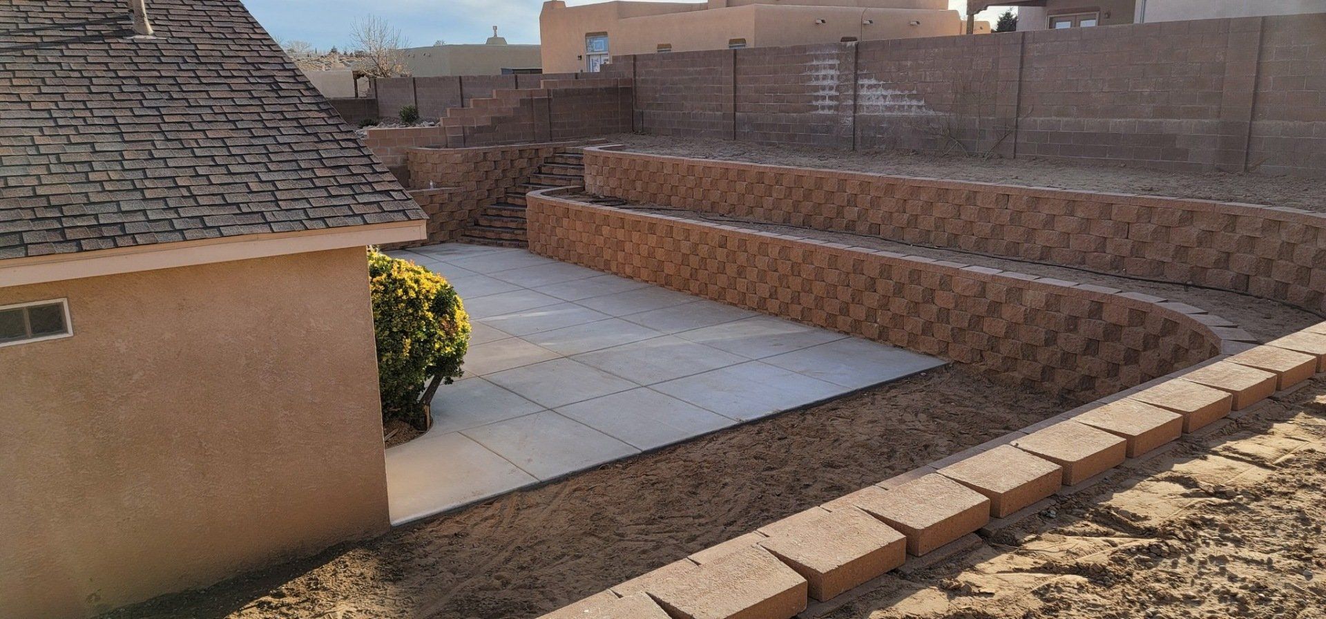 A brick wall is surrounding a patio in a backyard.