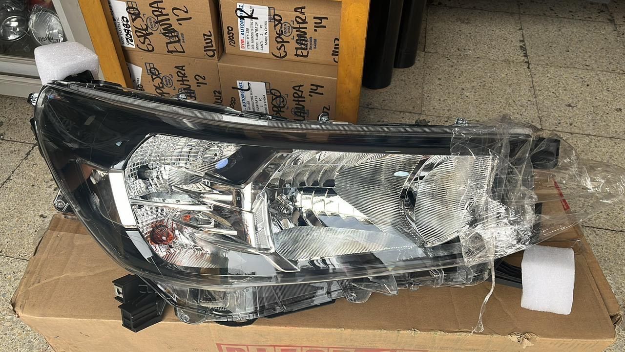 Faro de coche de color negro y plata, envuelto en plástico, apoyado sobre una caja de cartón.