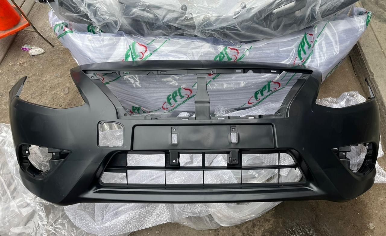 Parachoques de coche de color negro sobre superficie blanca, con parrilla central y aberturas para luces laterales.