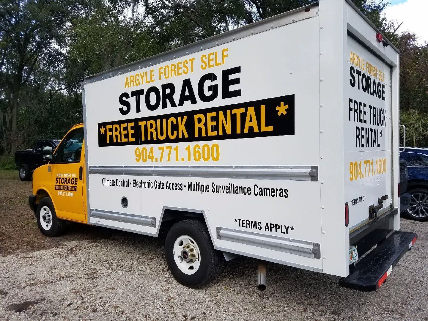 A yellow and white storage truck is parked in a gravel lot.