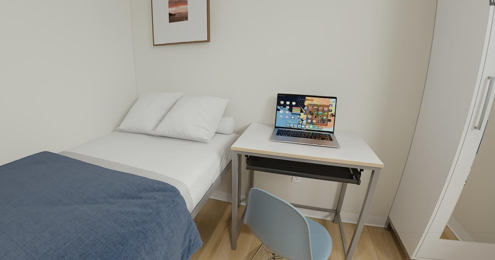 A bedroom with a single bed and a desk with a laptop on it.