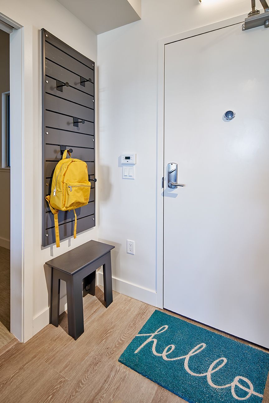 A hallway with a rug and a backpack hanging on the wall.