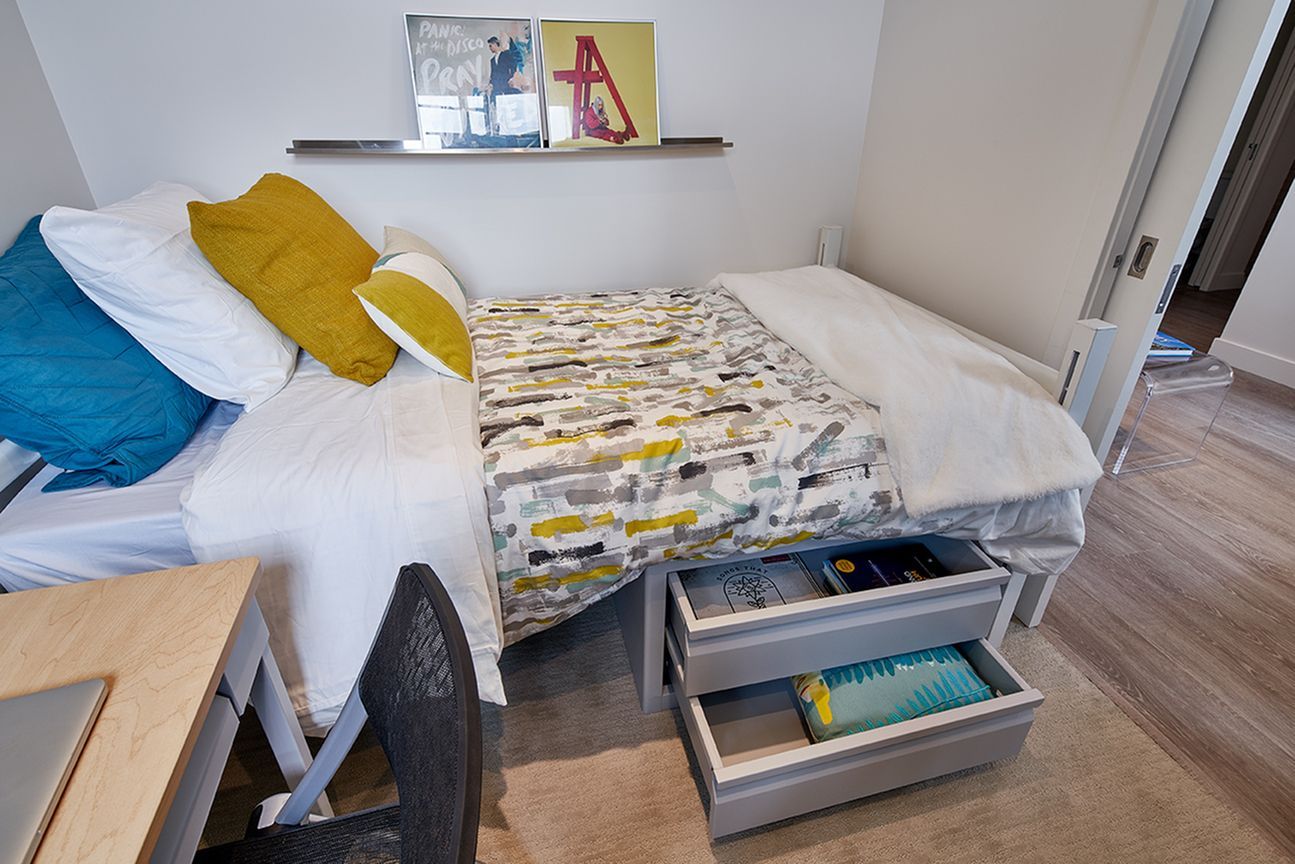 A bedroom with a bed , desk , chair and drawers.