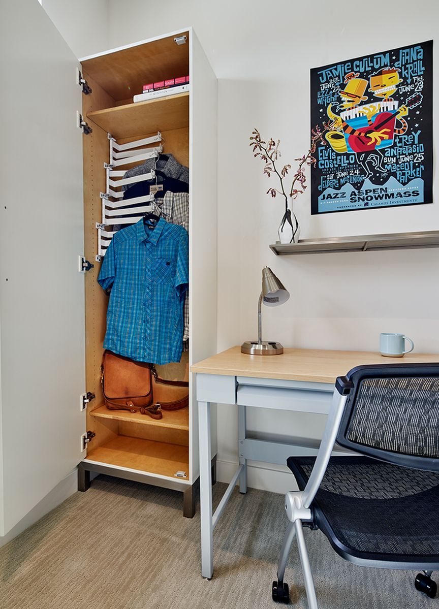 A room with a desk , chair , closet and a poster on the wall.