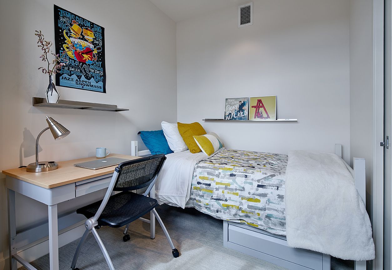 A bedroom with a bed , desk , chair and lamp.