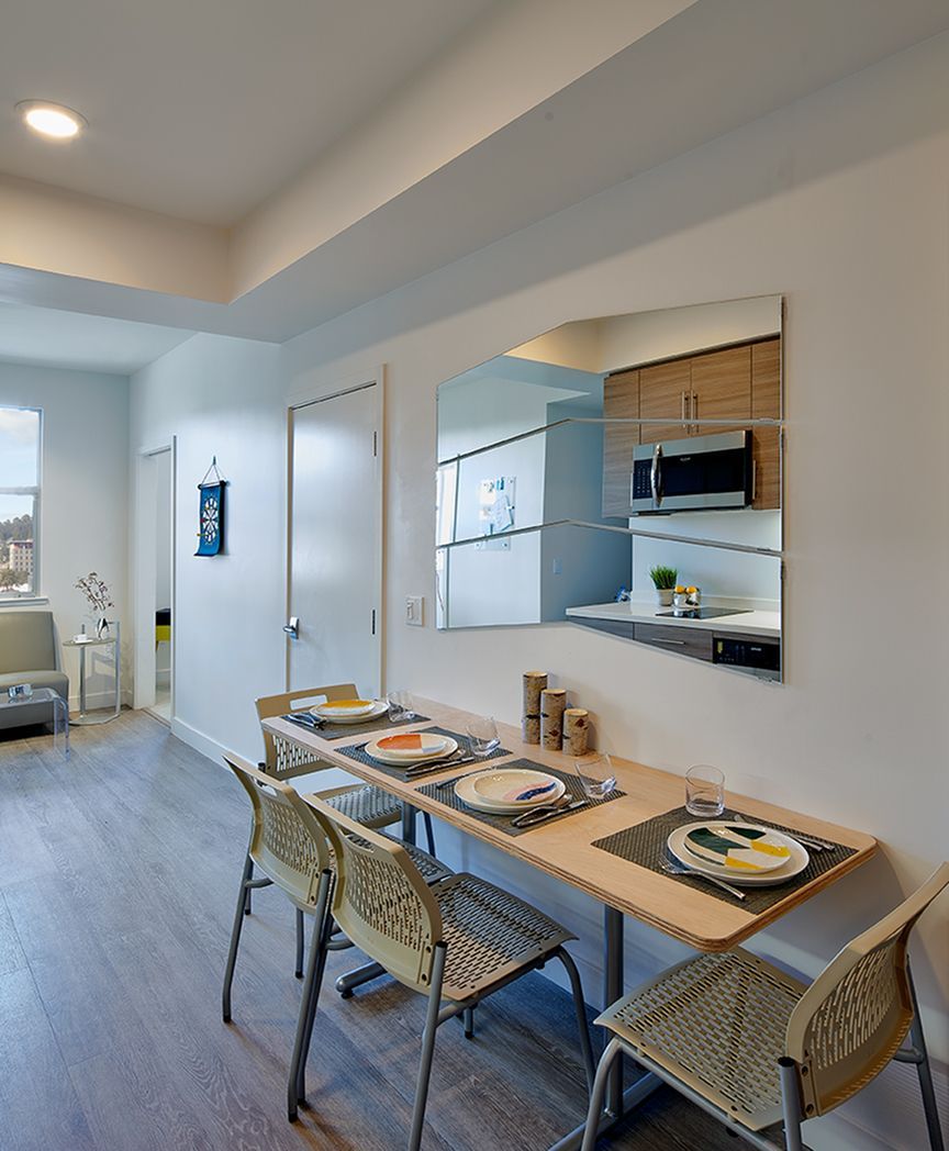 A dining room with a table and chairs and a mirror on the wall.
