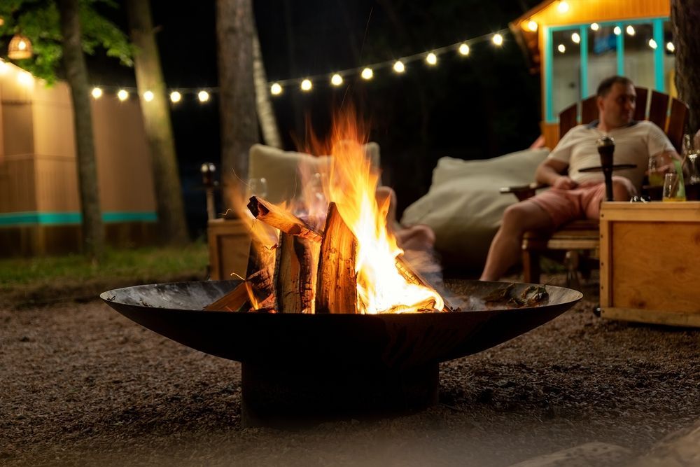 Backyard fire pit glowing under string lights, with a seated person and cozy outdoor seating nearby