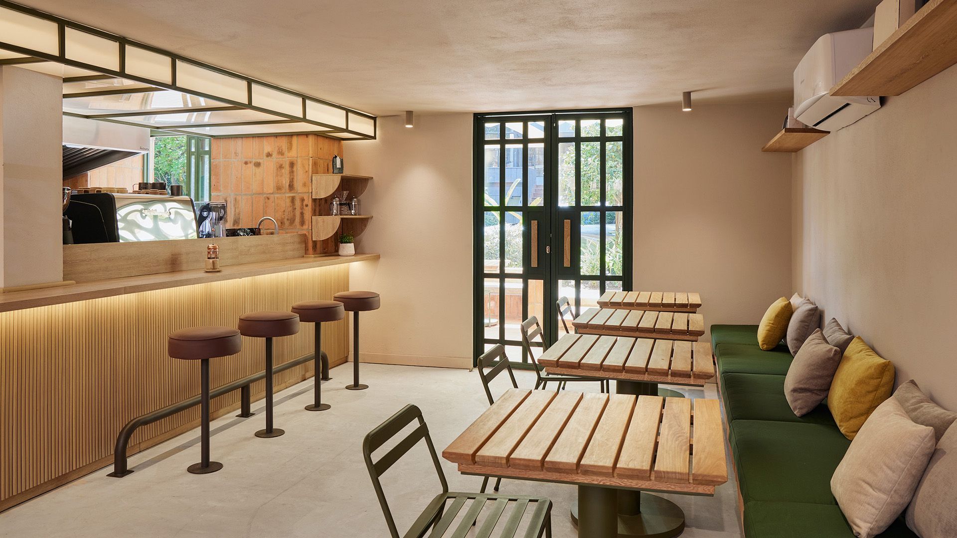 Cafetería interior con barra iluminada, taburetes modernos y mesas de madera, conectada al exterior