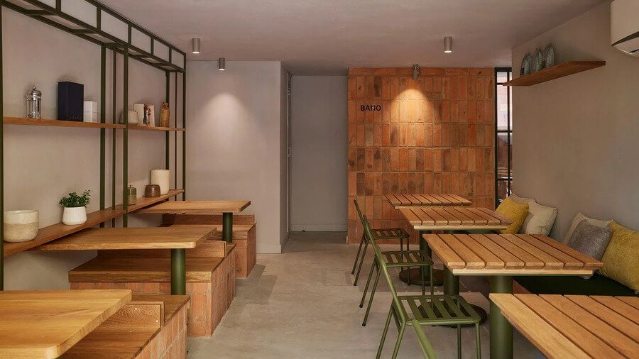 Comedor interior con mesas de madera y sillas verdes, decorado con estanterías minimalistas