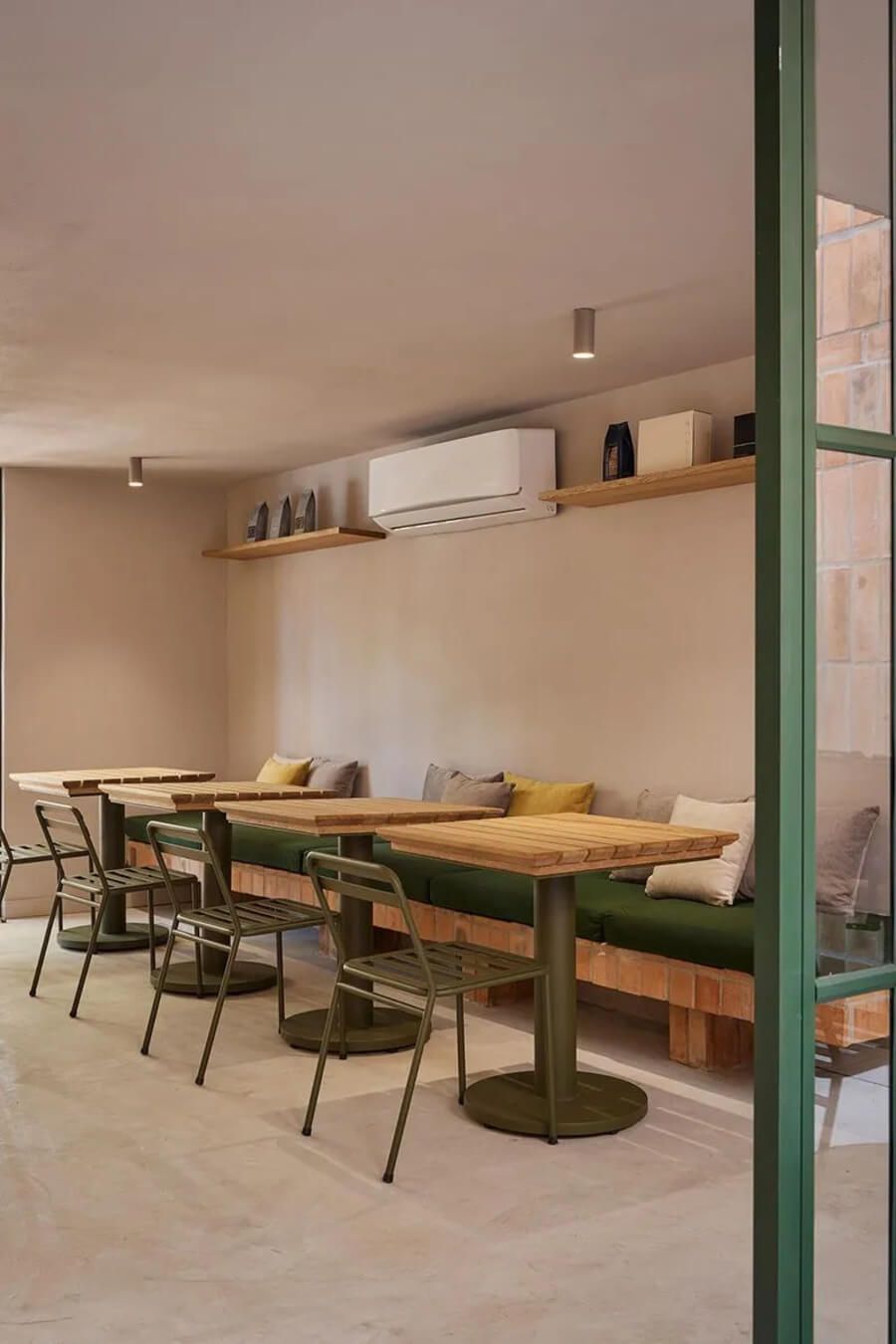 Espacio interior con mesas largas, sillas verdes y cojines en un ambiente acogedor