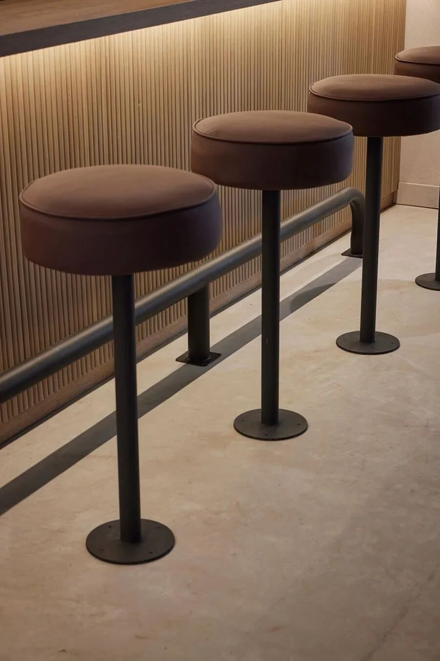 Taburetes altos de diseño moderno junto a una barra de madera iluminada