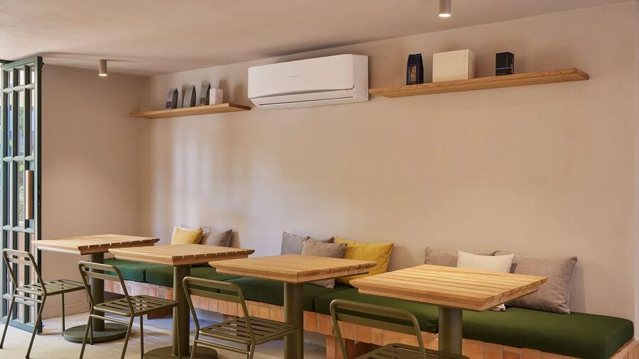 Comedor interior con mesas de madera, sillas verdes y asientos acolchados con cojines decorativos