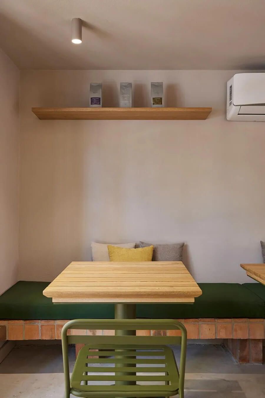 Espacio interior con mesa de madera, silla verde y cojines decorativos en un asiento acolchado