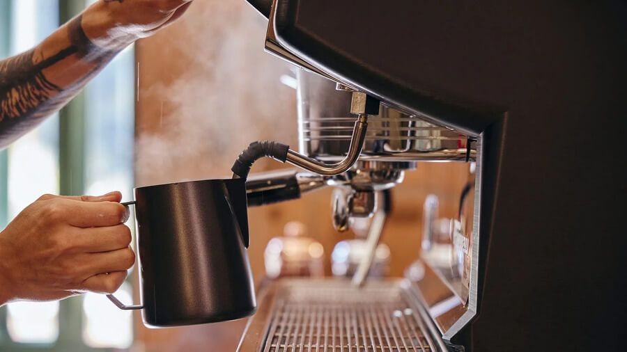 Mano usando una máquina de café espresso para preparar una bebida caliente