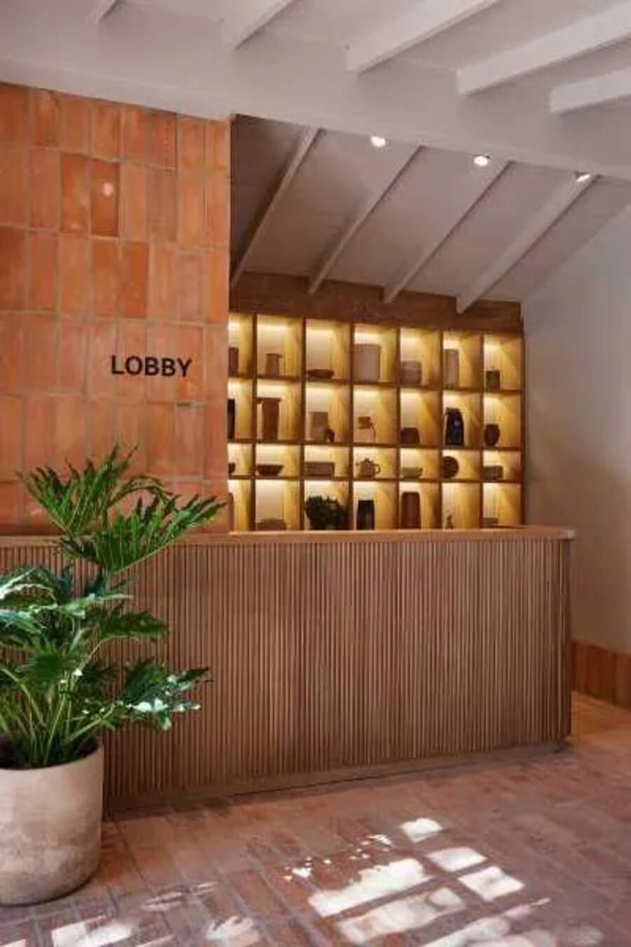 Recepción de hotel con pared de ladrillo, mostrador de madera y estantería iluminada
