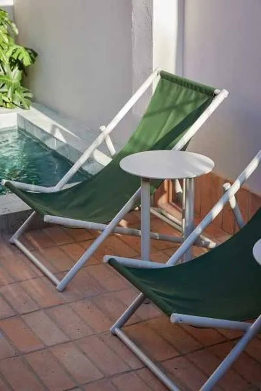 Sillas reclinables verdes junto a una pequeña mesa en un patio con piscina