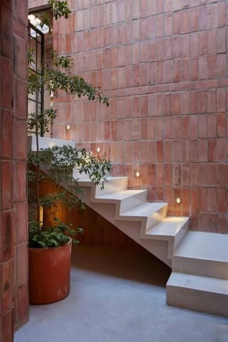 Escalera moderna con iluminación y pared de ladrillo en un ambiente decorado con plantas