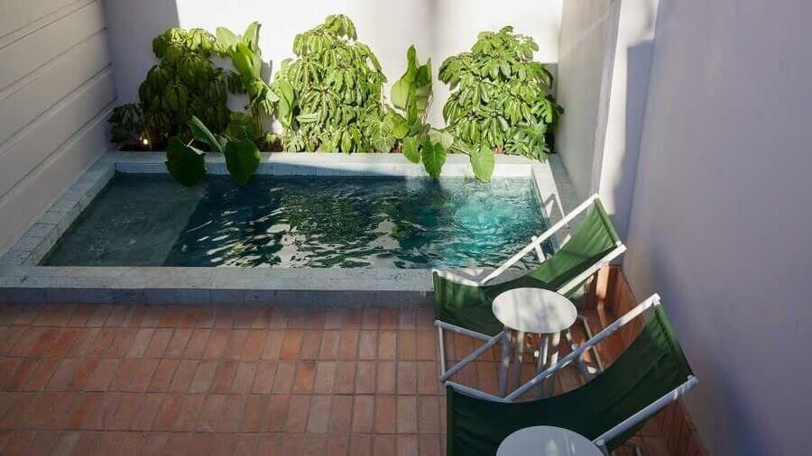 Pequeña piscina rodeada de vegetación con sillas reclinables y mesa en un patio tranquilo