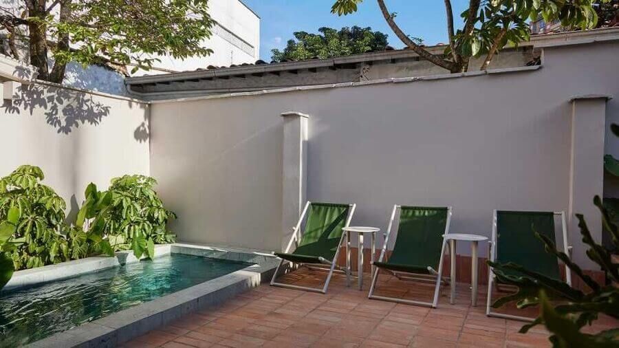 Patio con piscina pequeña, sillas reclinables verdes y ambiente soleado rodeado de vegetación