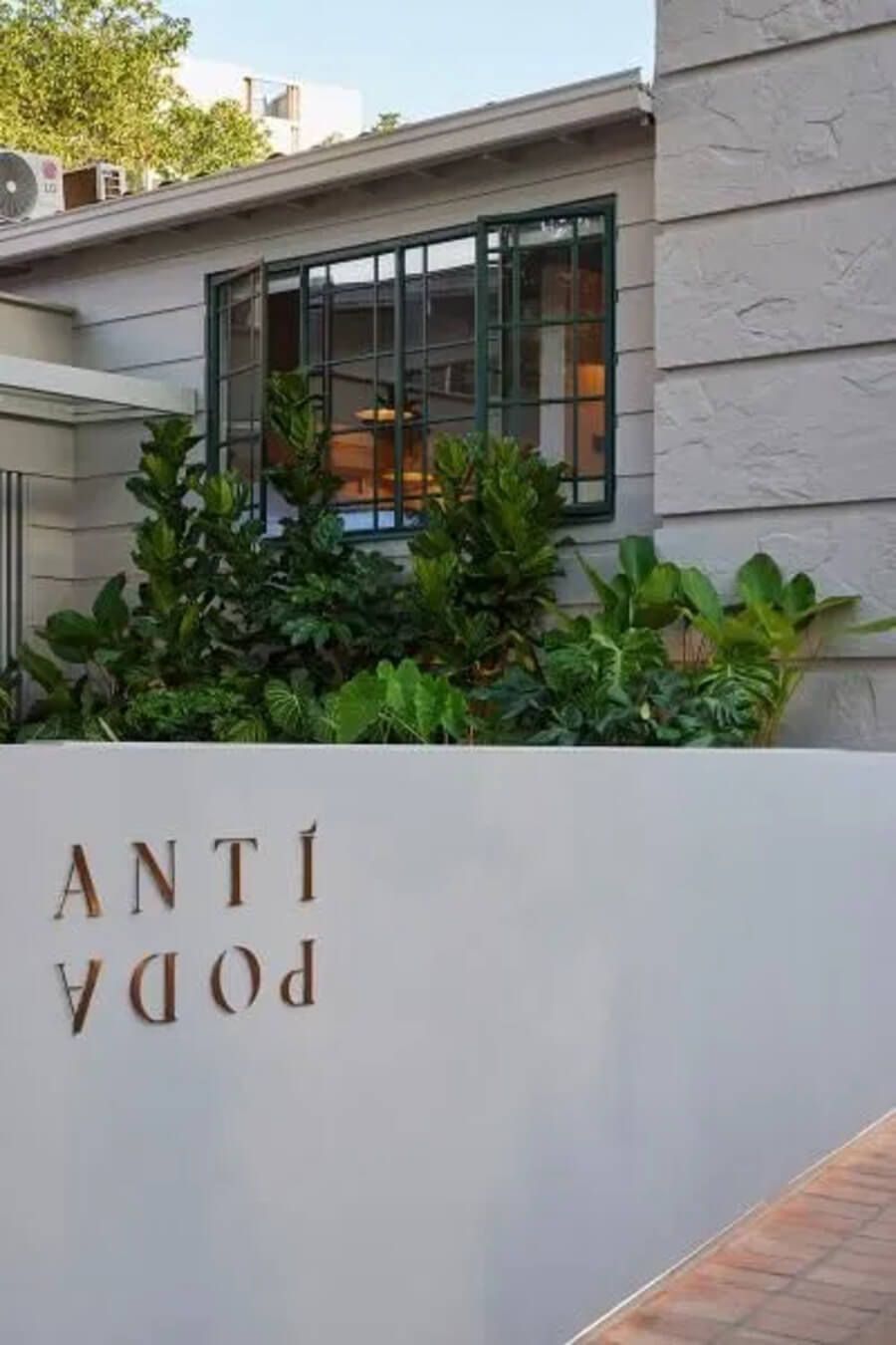 Detalle del logo del hotel Antípoda con jardín decorativo y fachada moderna