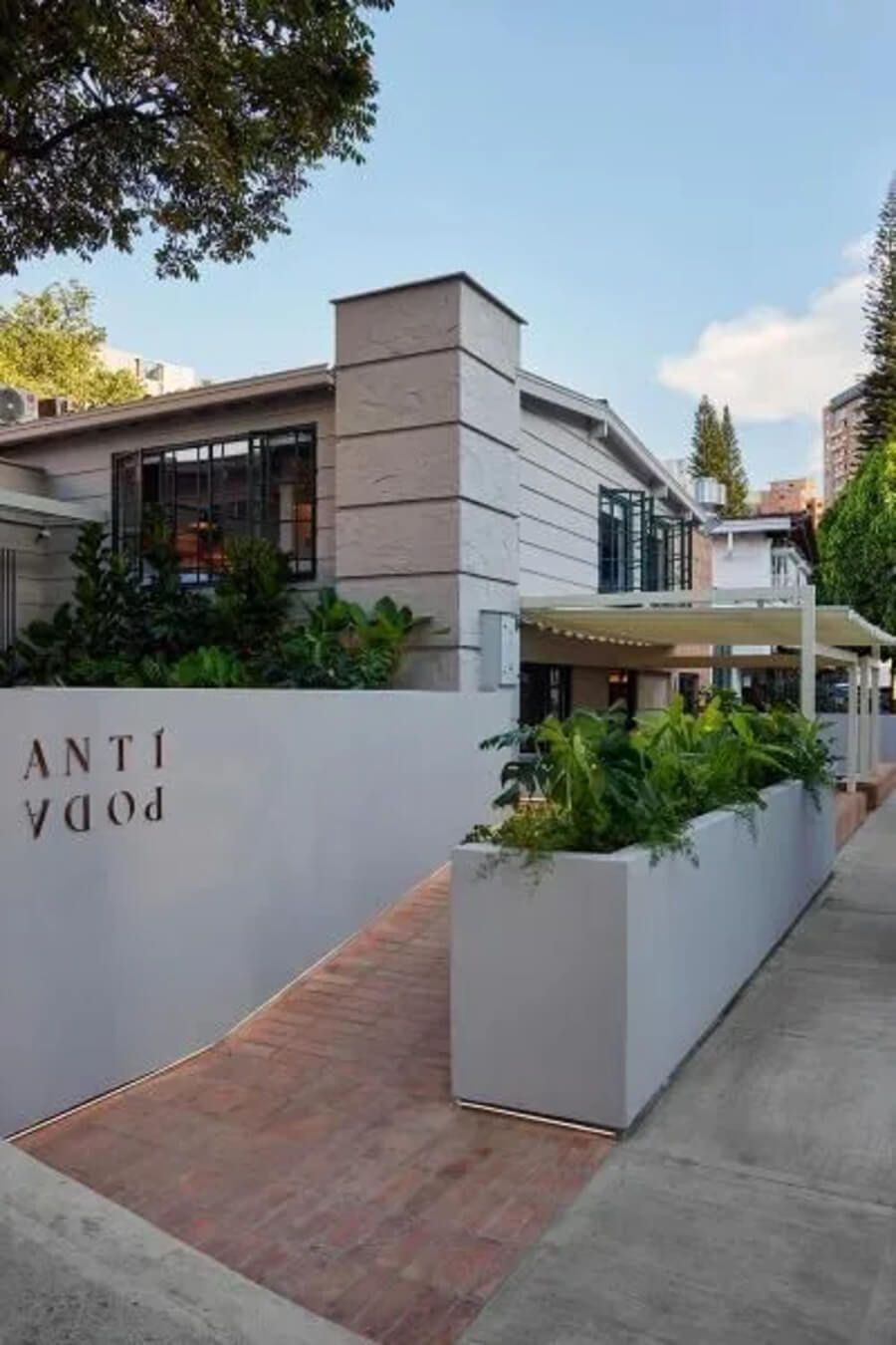 Entrada del hotel Antípoda con diseño moderno y jardineras llenas de vegetación