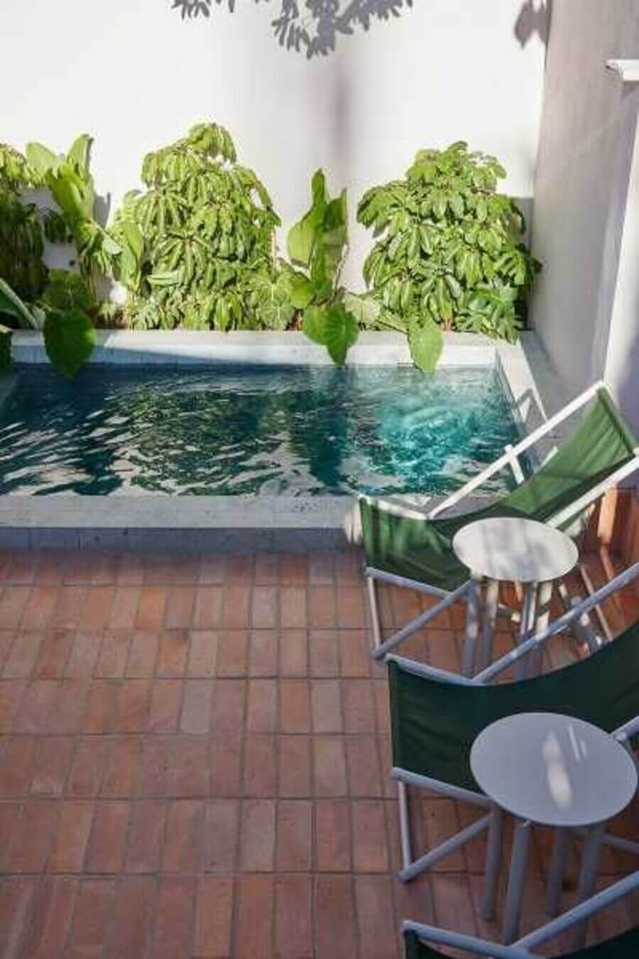 Patio con piscina rodeada de plantas, sillas reclinables verdes y mesas pequeñas
