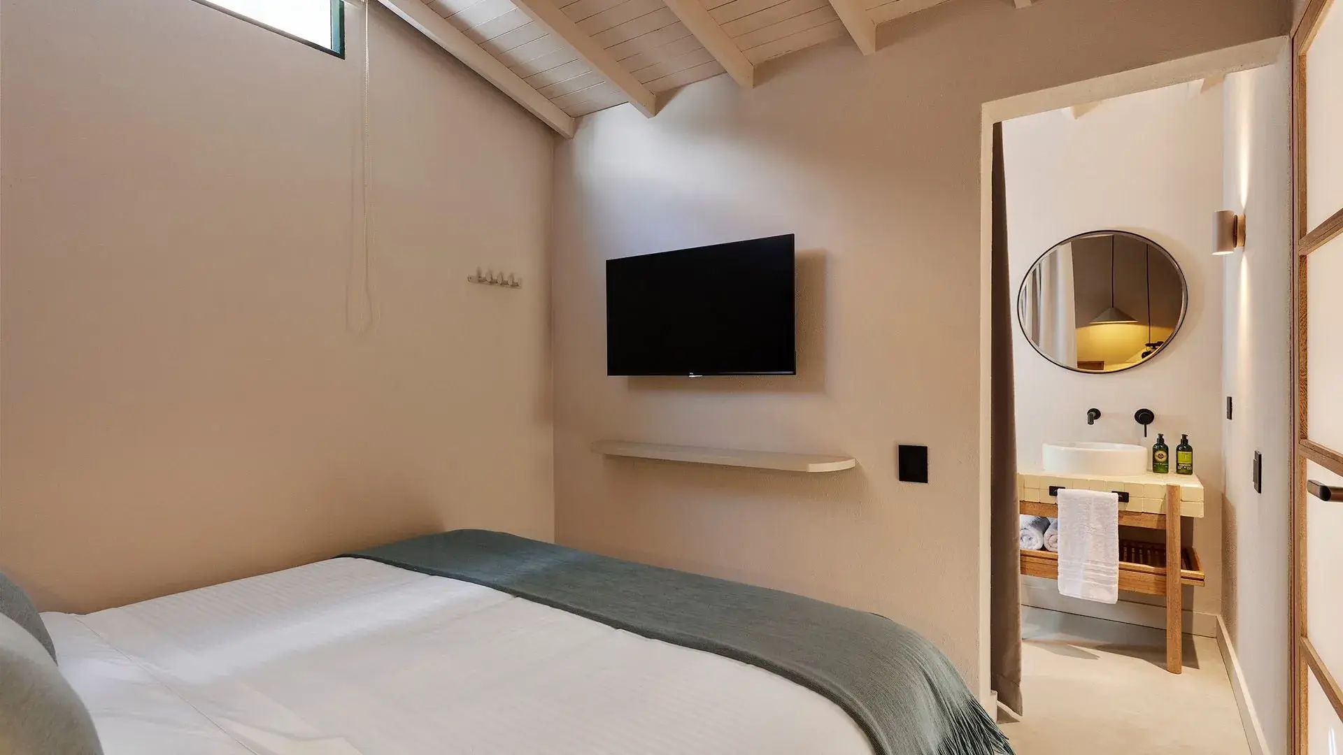 Dormitorio de lujo en la habitación Sulu, con cama confortable, televisión de pantalla plana y baño moderno con espejo redondo, ideal para una estancia elegante y cómoda.