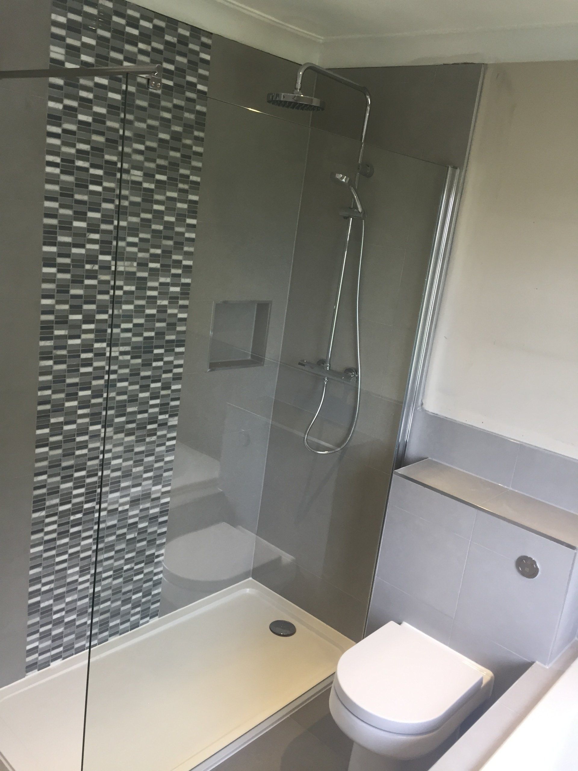 Modern bathroom with shower, toilet, and gray tiles. Decorative tiled accent wall.