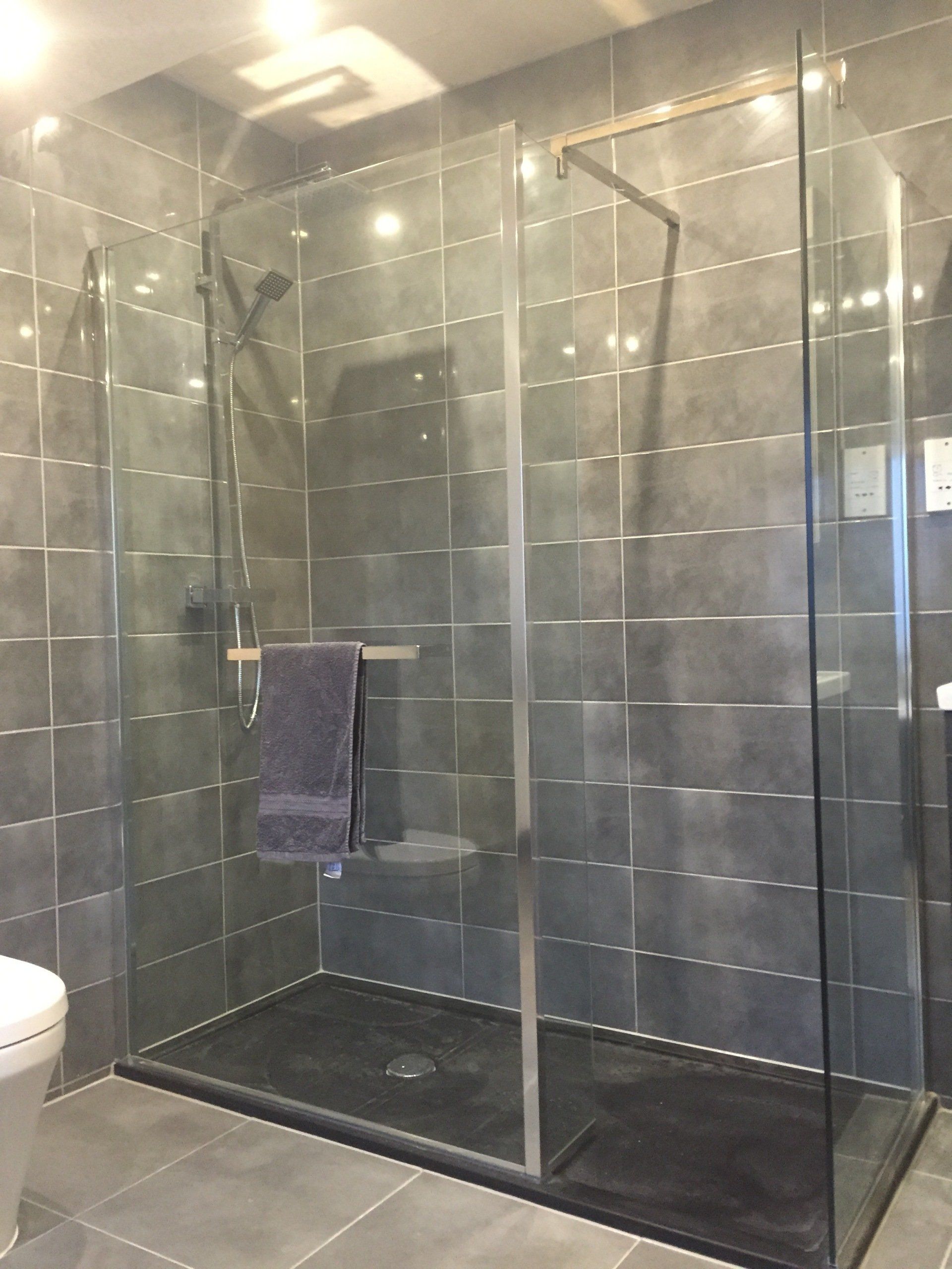 Glass shower enclosure with gray tiled walls and floor. A towel hangs on a bar inside the shower.
