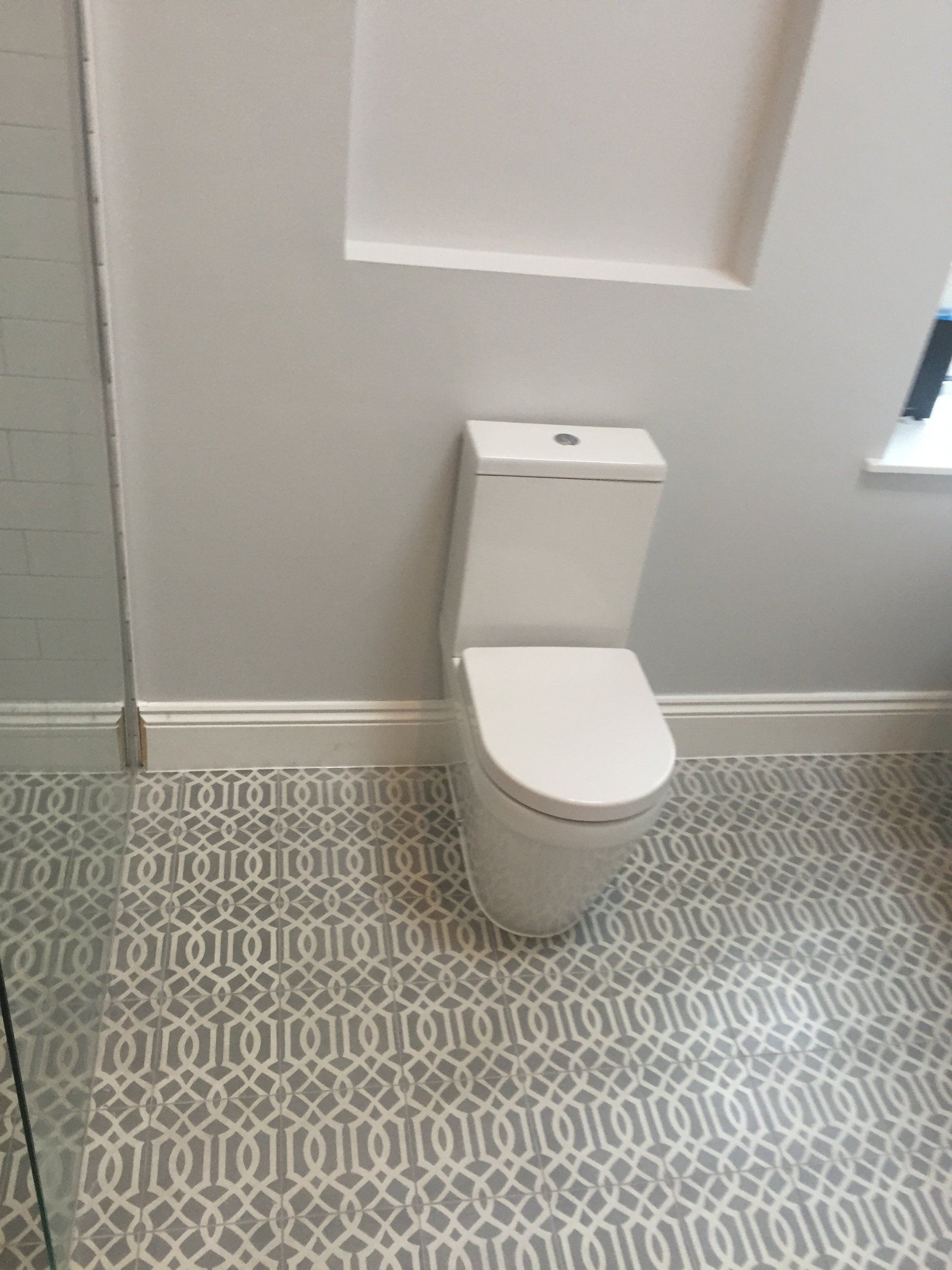 White toilet in a bathroom with patterned gray and white tile floor.