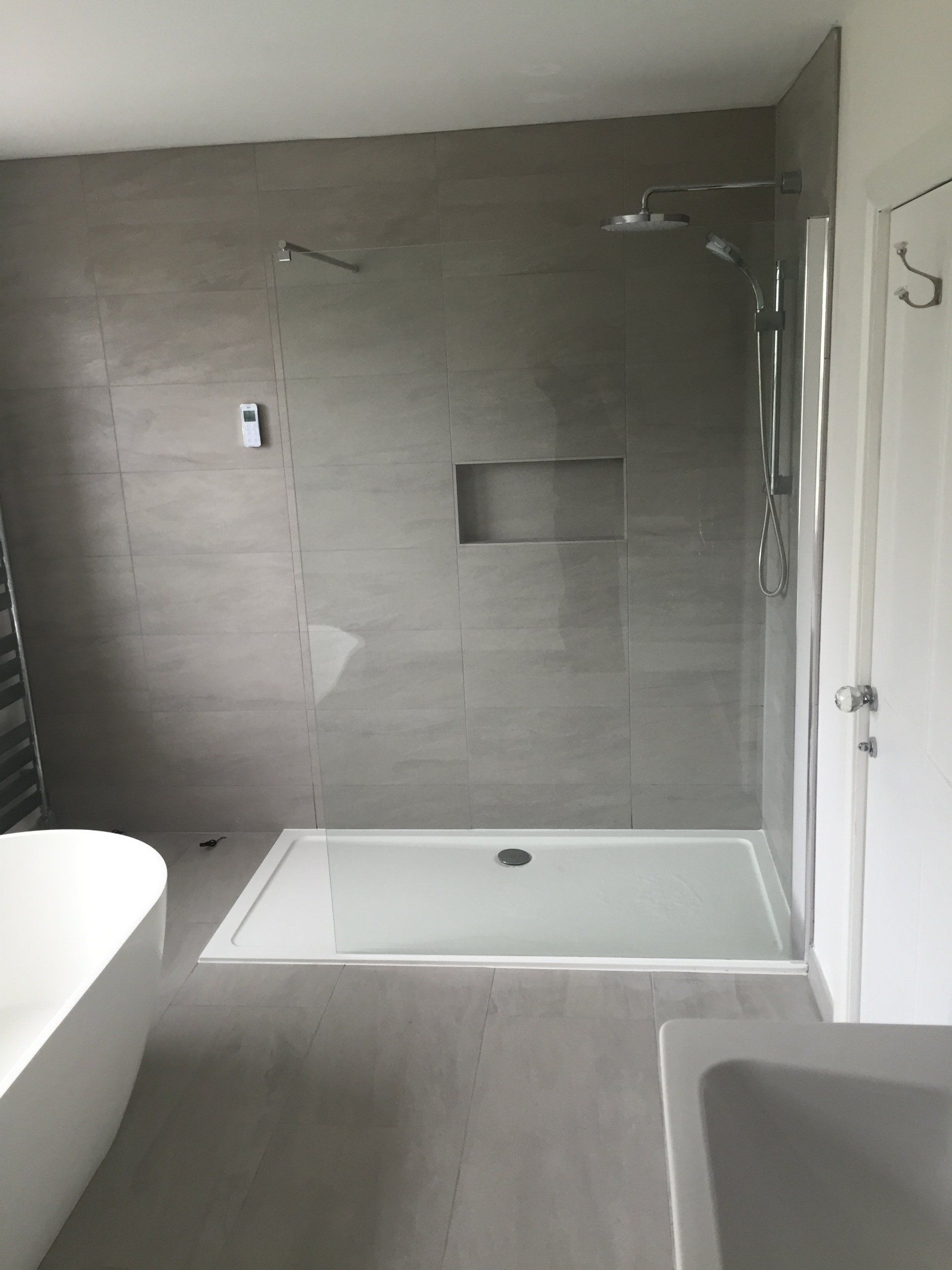 Modern bathroom with gray tiled walls, glass shower, and white fixtures.